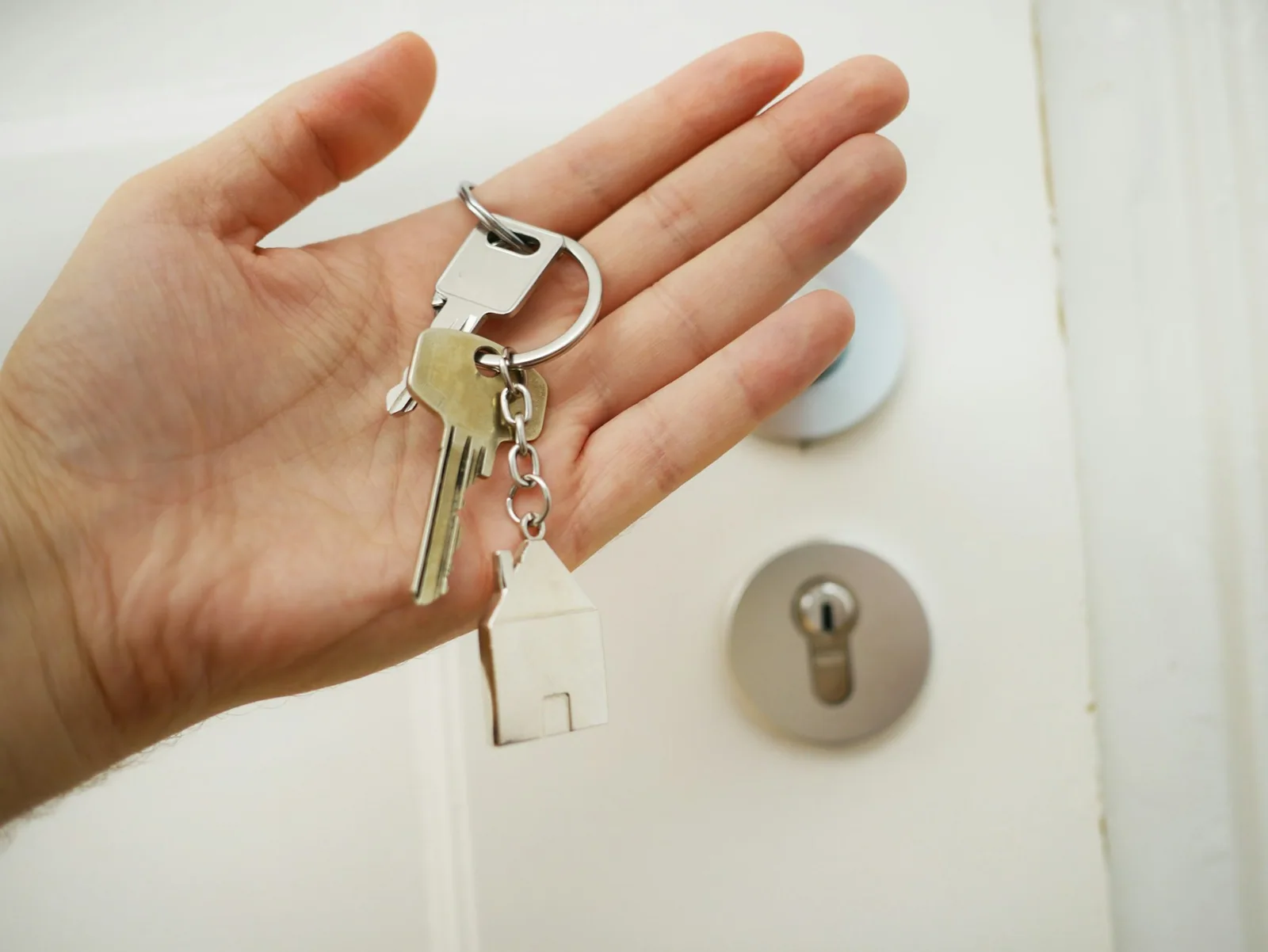A hand holding house keys beside a door lock